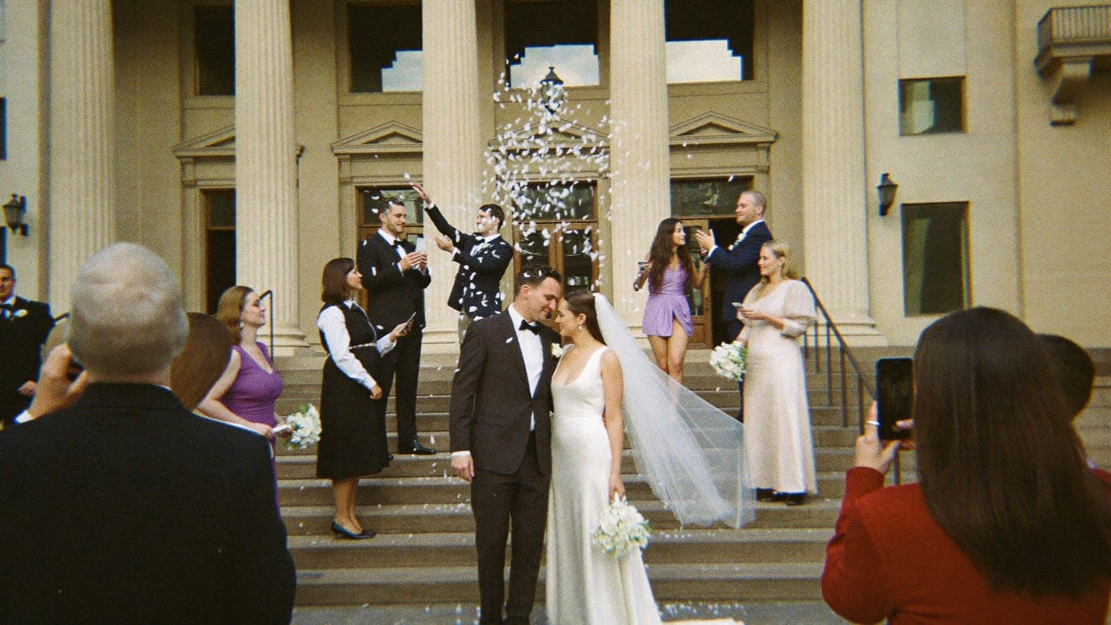 A small wedding party throwing confetti over the couple on the steps of city hall
