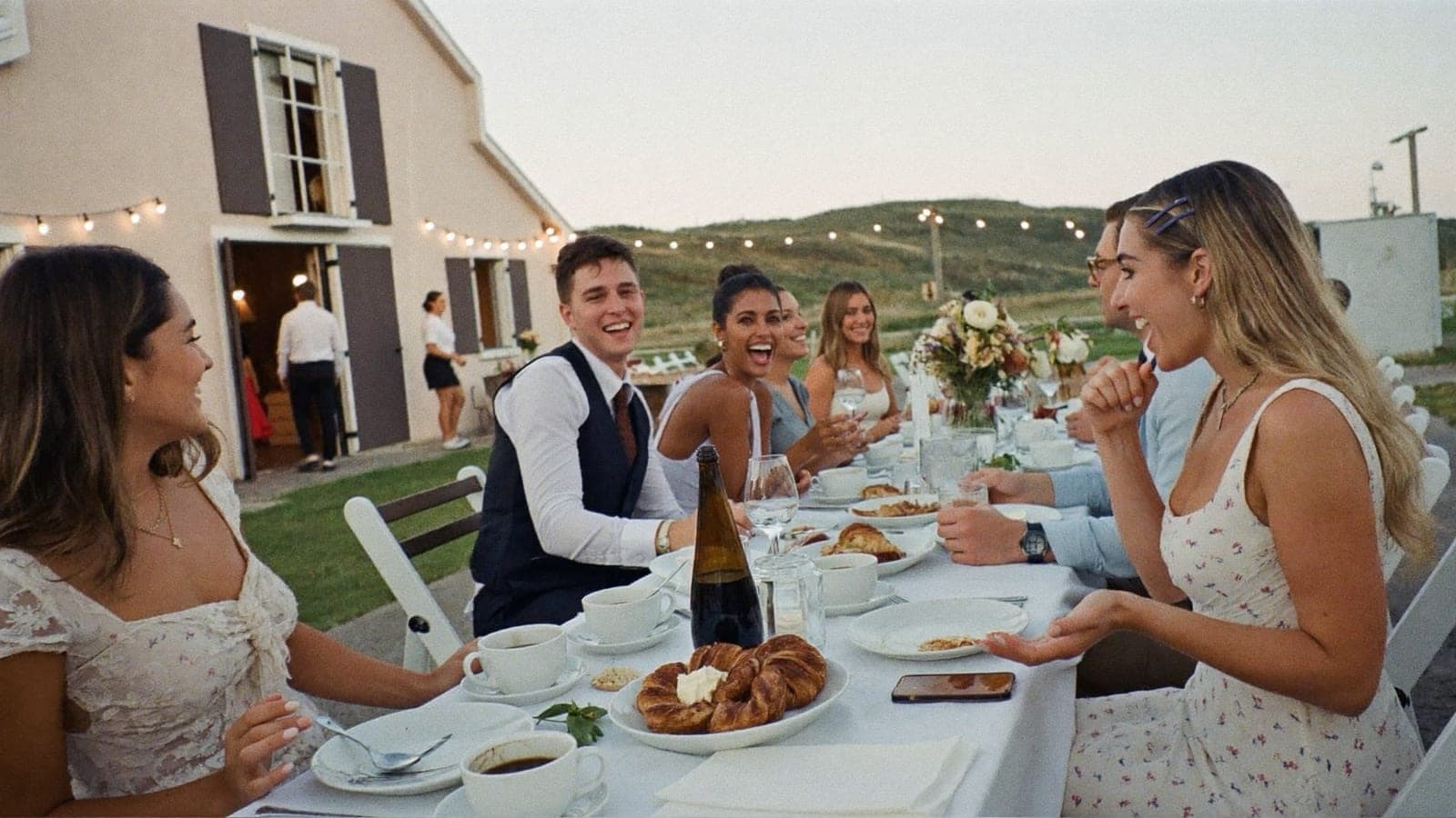 Friends and the newlyweds at a long outdoor brunch table the day after the wedding