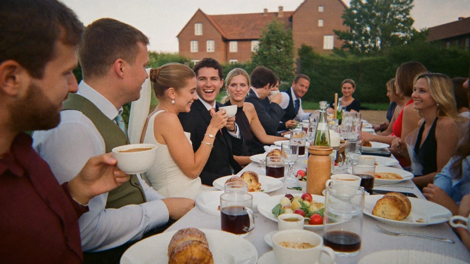 Freunde und das Brautpaar beim Brunch an einer langen Tafel draußen, am Tag nach der Hochzeit
