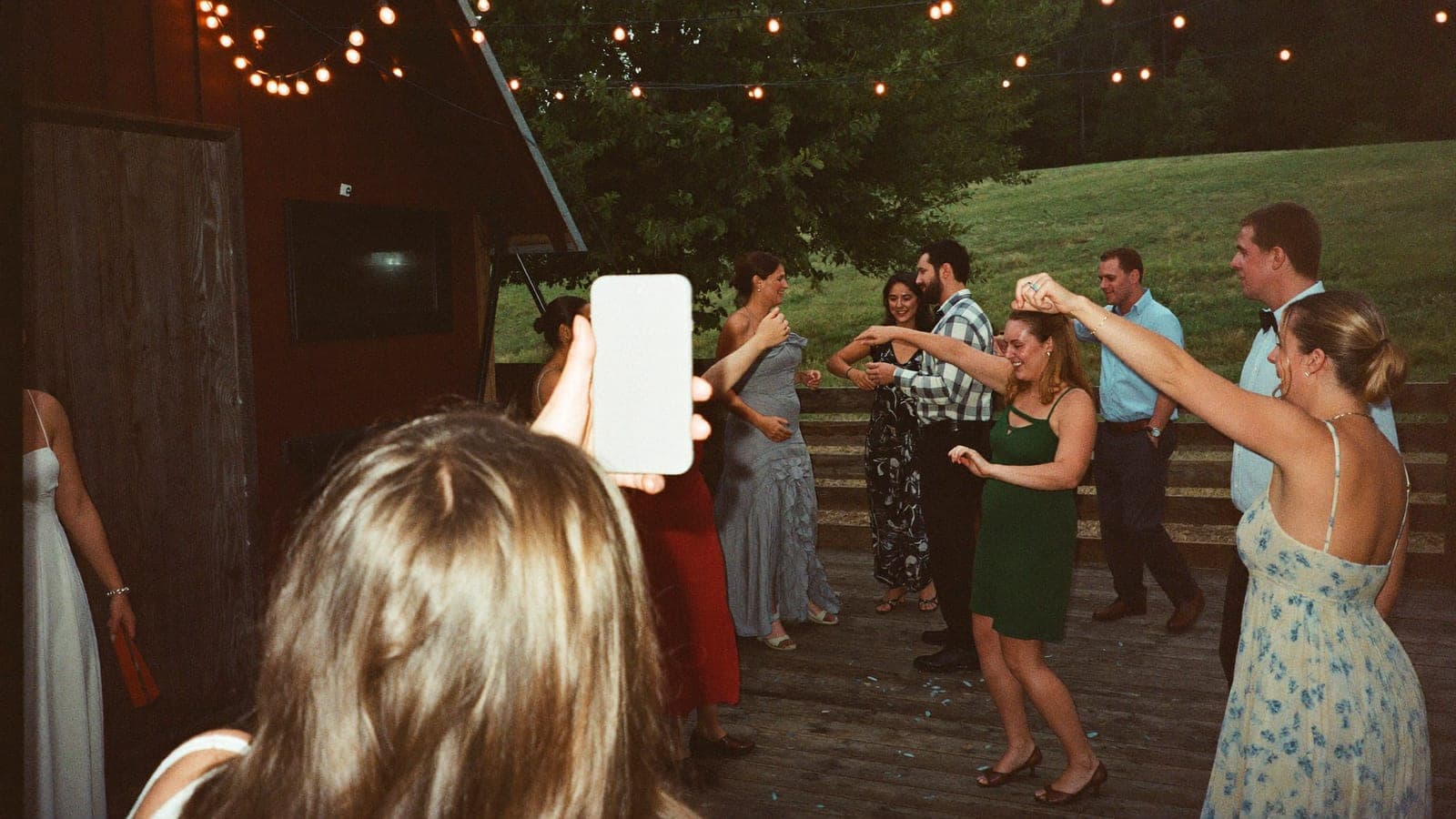A wedding guest takes a flash photo of friends dancing, using a phone