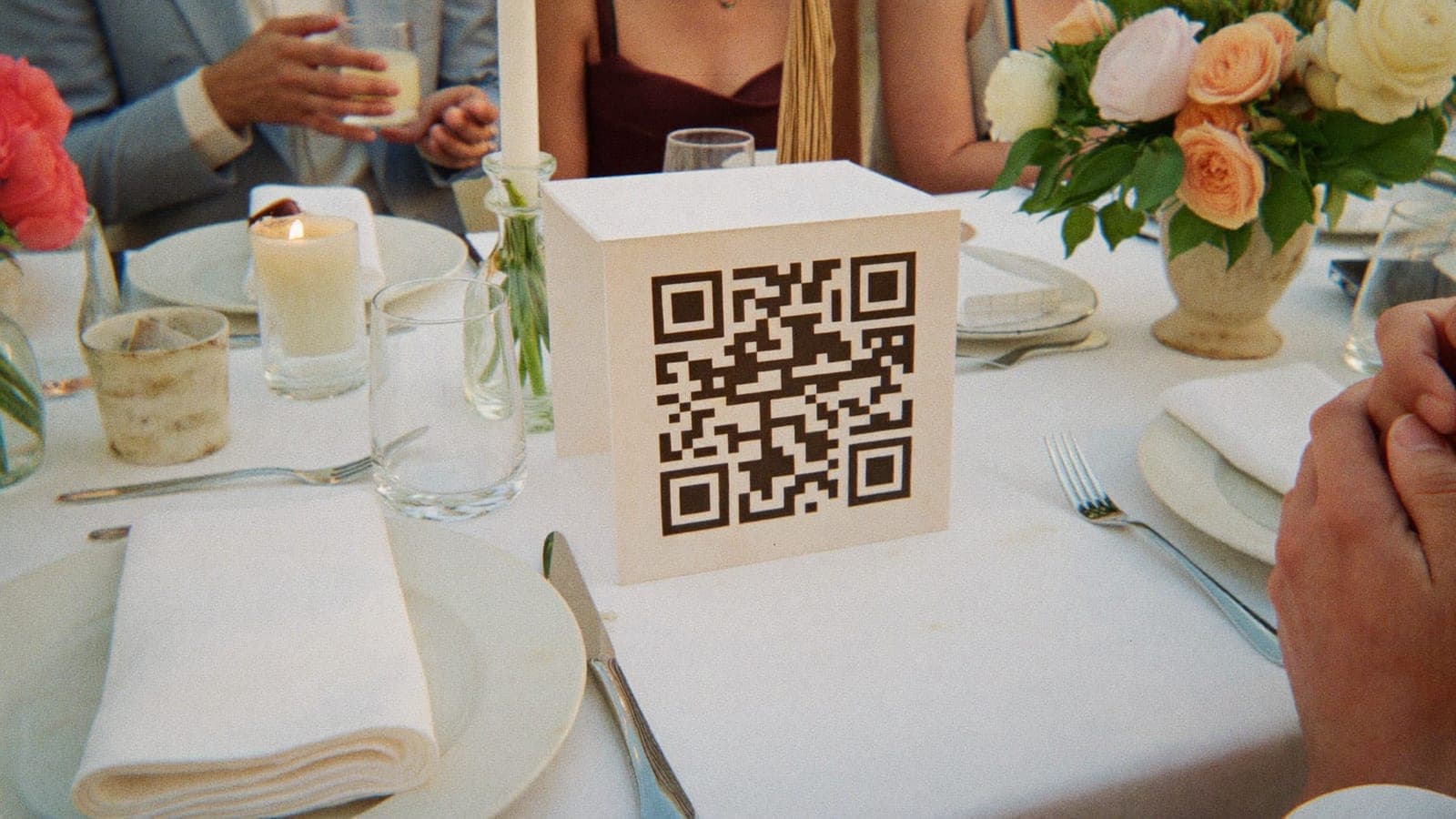 Un cartel de mesa con código QR entre los platos y las flores de una mesa de boda
