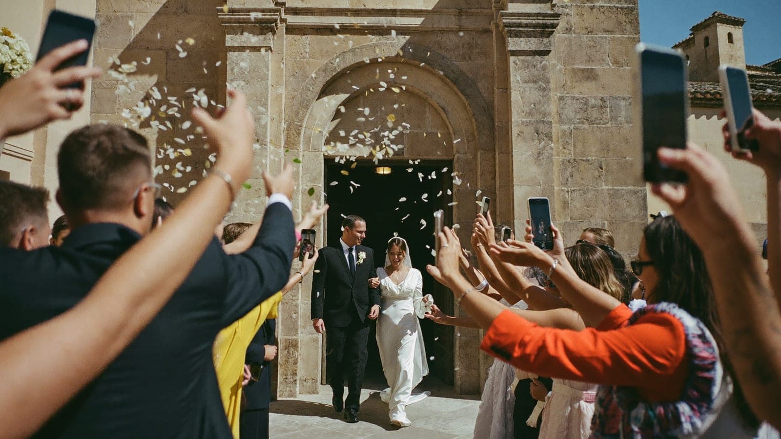 Los novios salen de la iglesia mientras los invitados lanzan arroz y hacen fotos