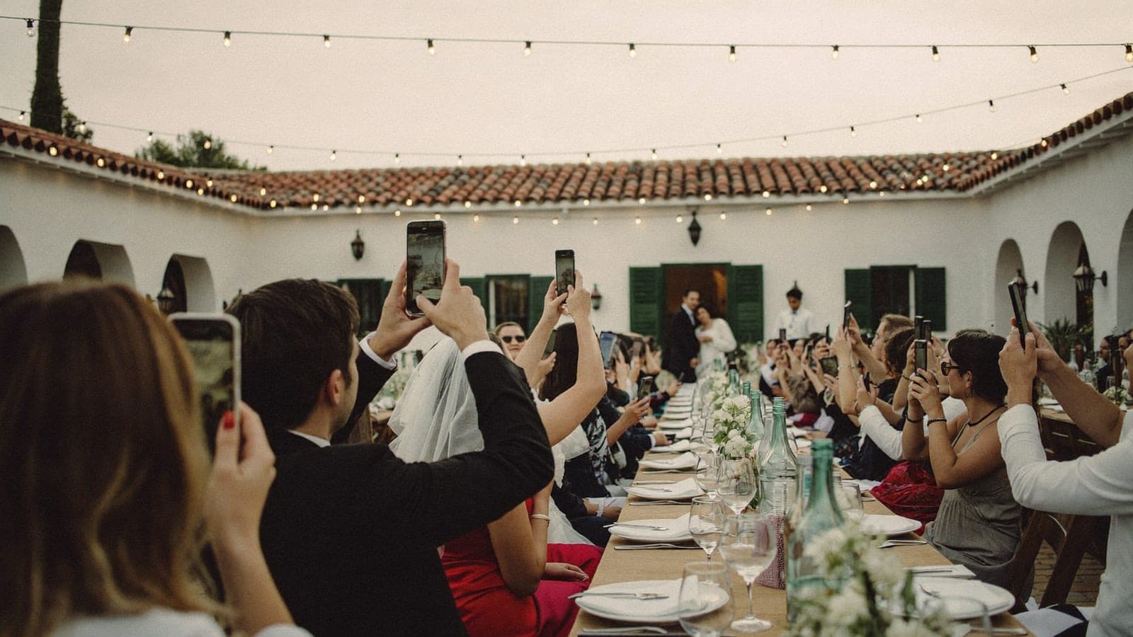 Los invitados en la mesa levantan sus móviles cuando los novios entran en el salón