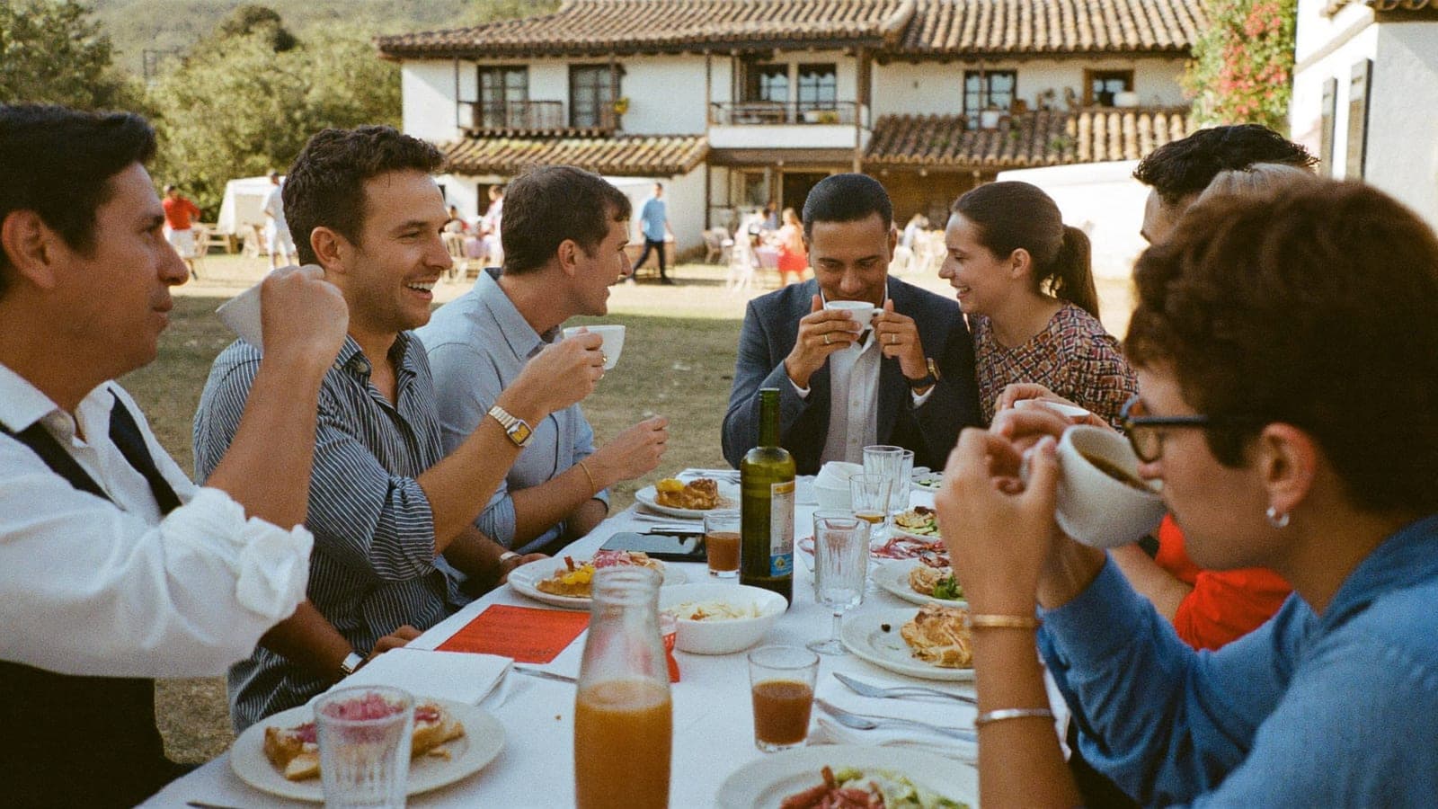 Amigos y los novios en una larga mesa de brunch al aire libre, el día después de la boda