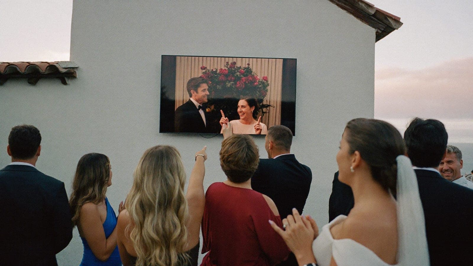 Los invitados señalan riendo una foto de un invitado en la pantalla grande