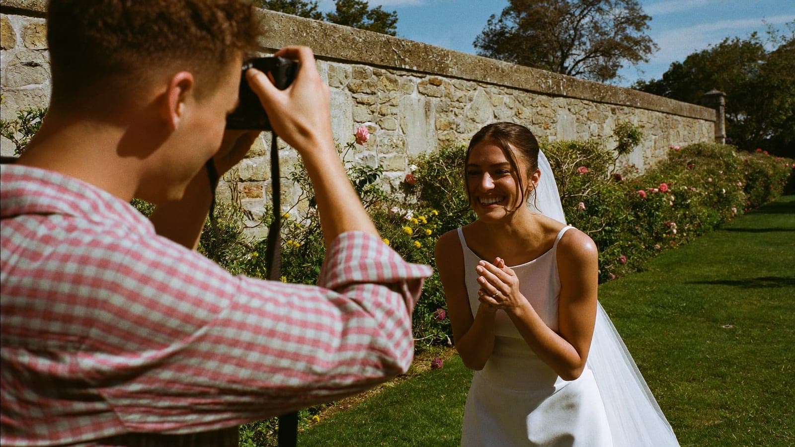 Un ami des mariés photographie la mariée qui rit avec un reflex dans le jardin d'un domaine