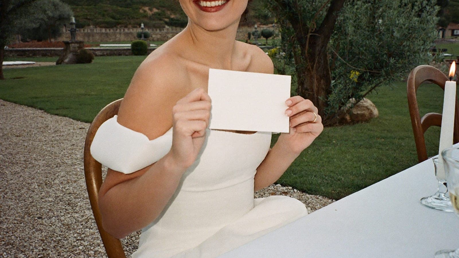 La mariée tient un petit carton à sa table, dans le jardin d'un domaine, pendant le dîner de mariage