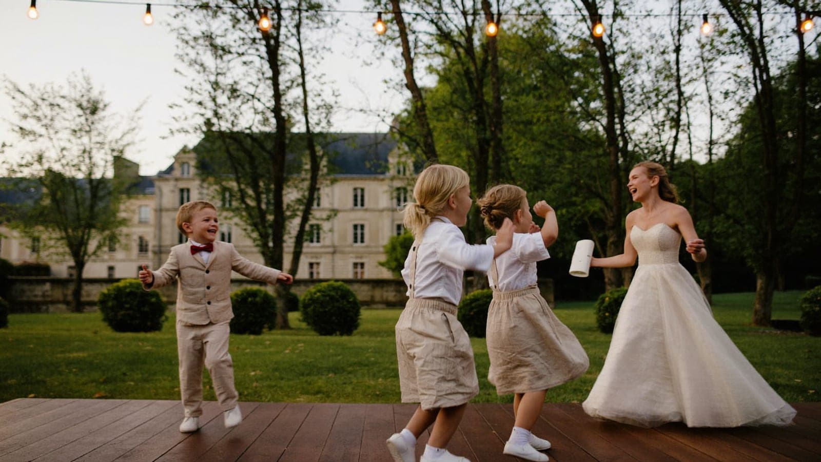 Des enfants dansent avec la mariée sur la piste de danse, sous les guirlandes lumineuses