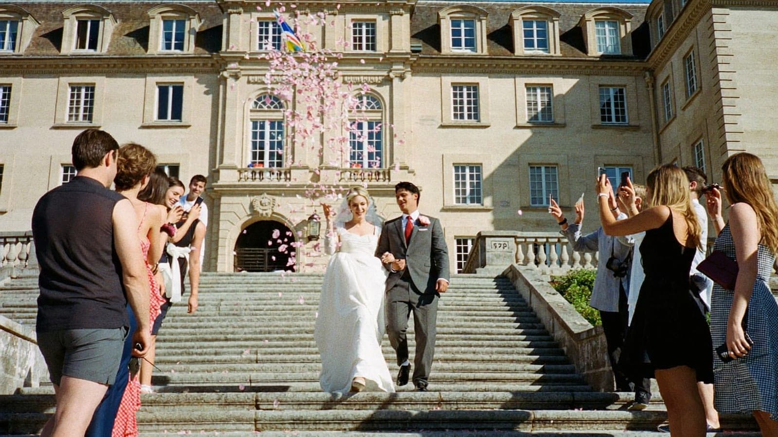 Les mariés descendent les marches de la mairie sous une pluie de pétales, les invités photographient