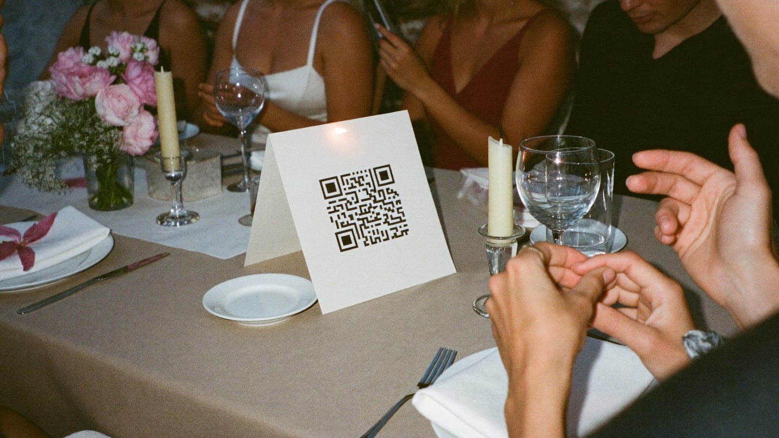Un chevalet avec QR code entre les assiettes et les fleurs d'une table de mariage