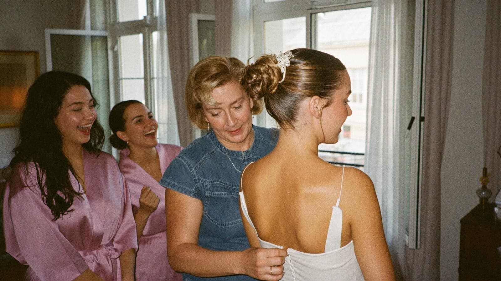 La mère de la mariée ferme les boutons de la robe près de la fenêtre