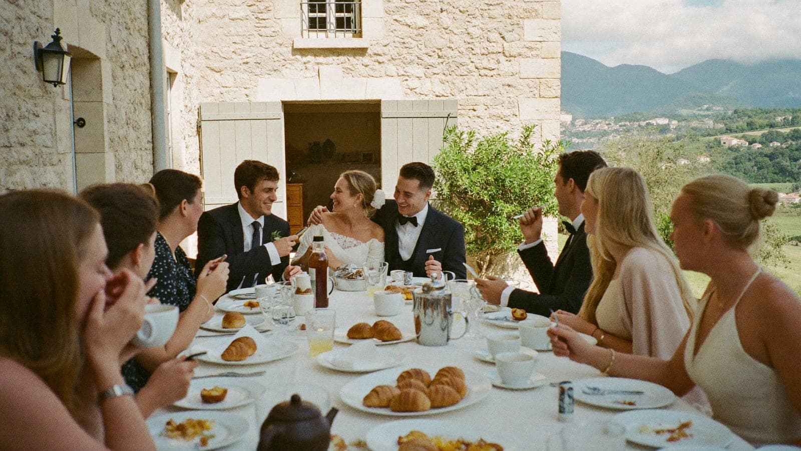 Des amis et les mariés autour d'une longue table de brunch dehors, le lendemain du mariage