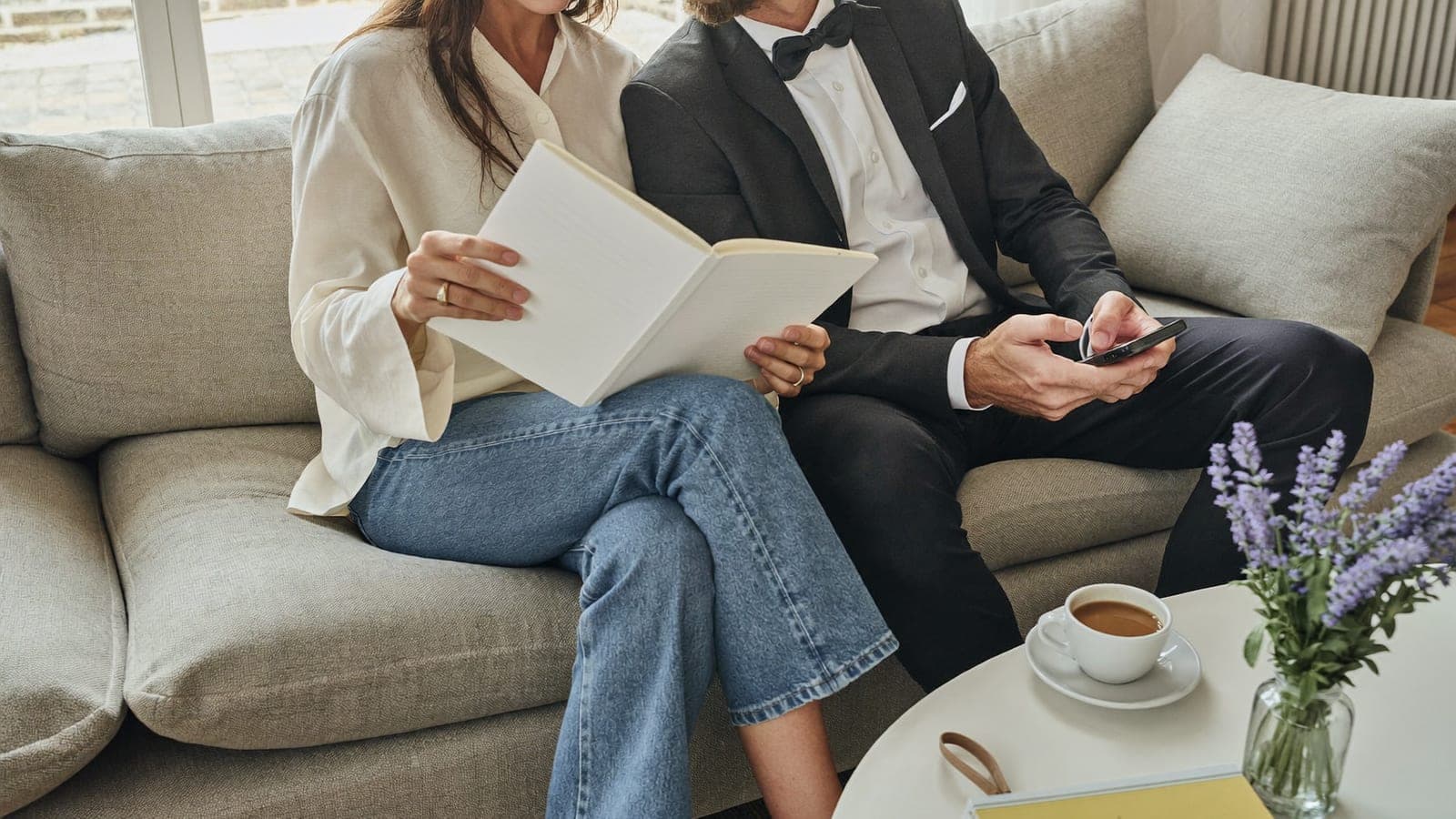 Un couple fiancé prépare son mariage sur le canapé avec un carnet et un téléphone