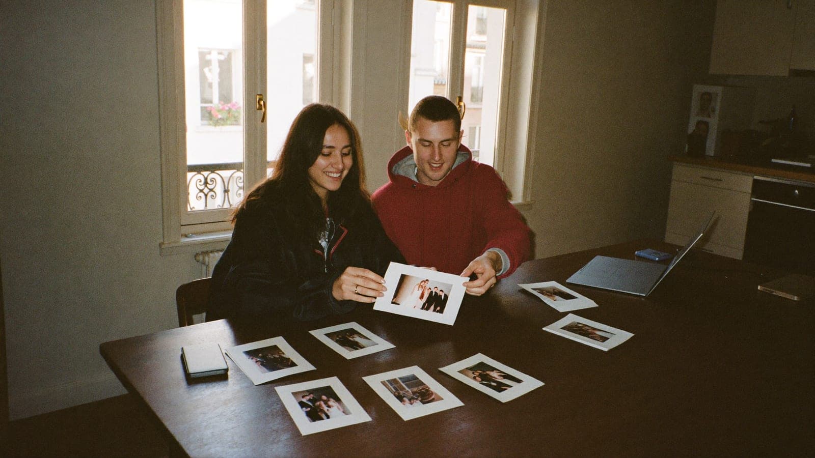 Des photos de mariage imprimées triées sur la table de la cuisine, à côté d'un disque dur externe