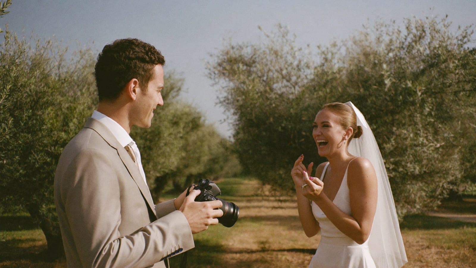 Un amico degli sposi fotografa la sposa che ride con una reflex in giardino