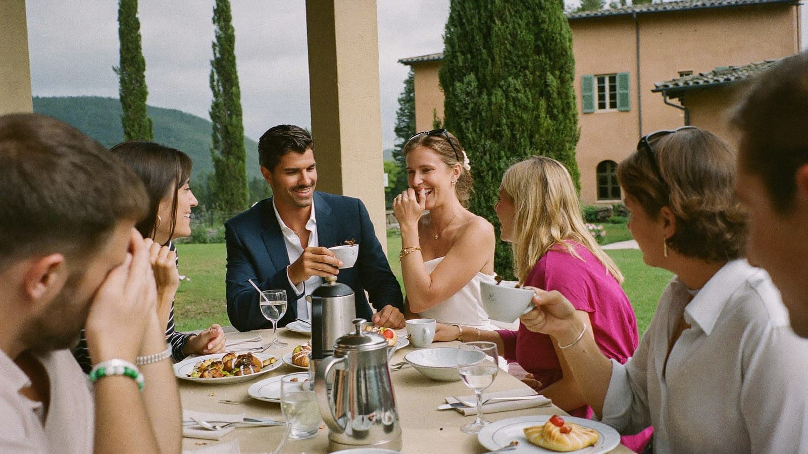 Amici e sposi a un lungo tavolo per il brunch all'aperto, il giorno dopo il matrimonio