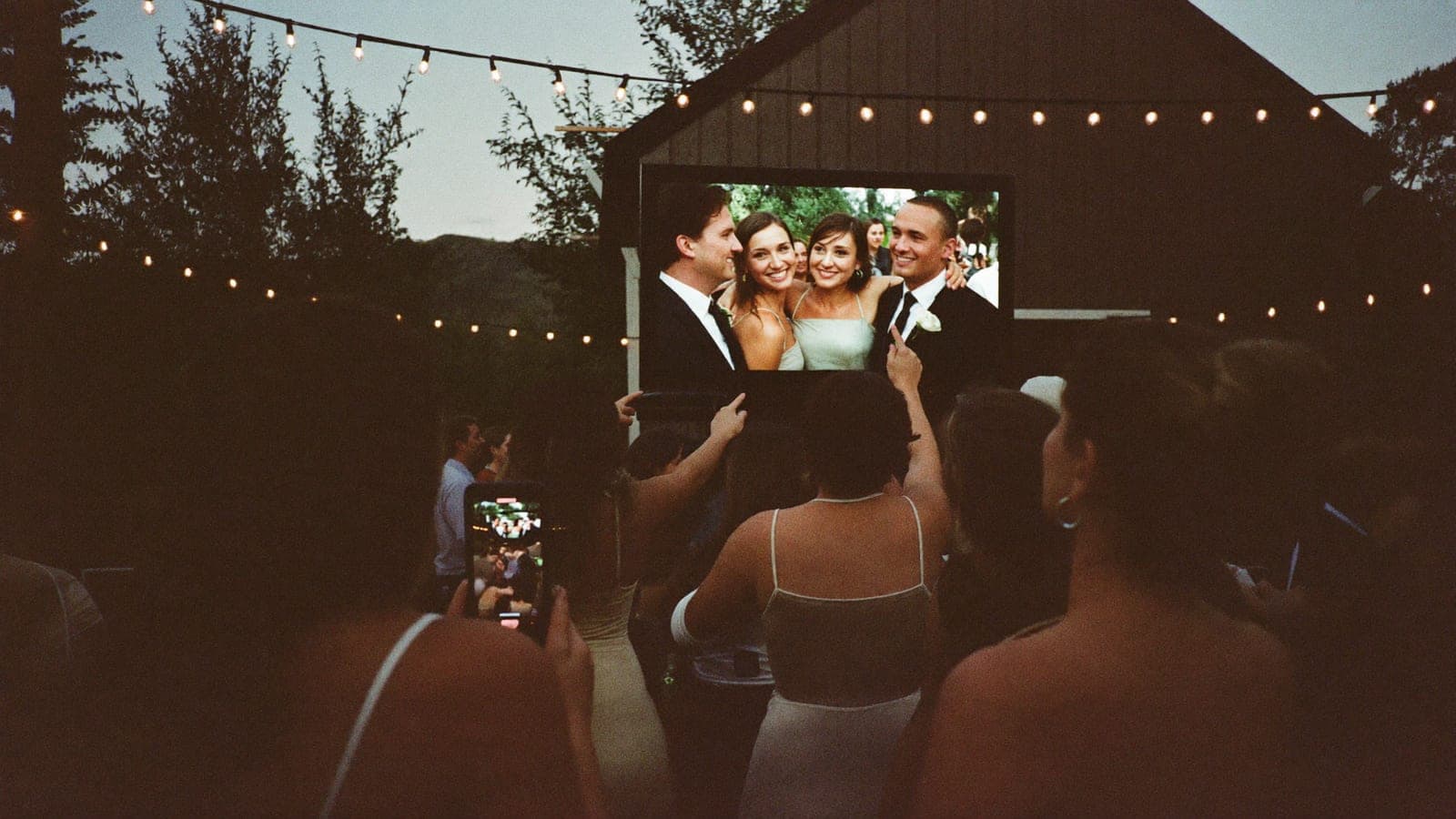 Wedding guests point and laugh at a guest photo on the big screen