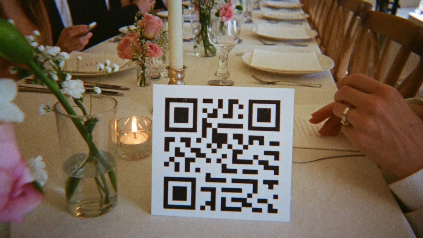 Tabliczka z kodem QR między talerzami i kwiatami na weselnym stole