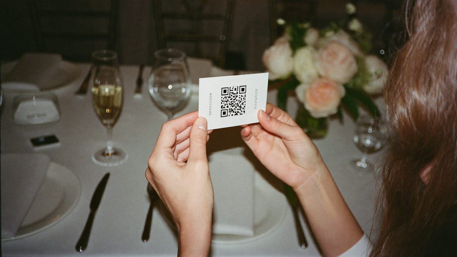 Гостья за свадебным столом держит карточку с QR-кодом