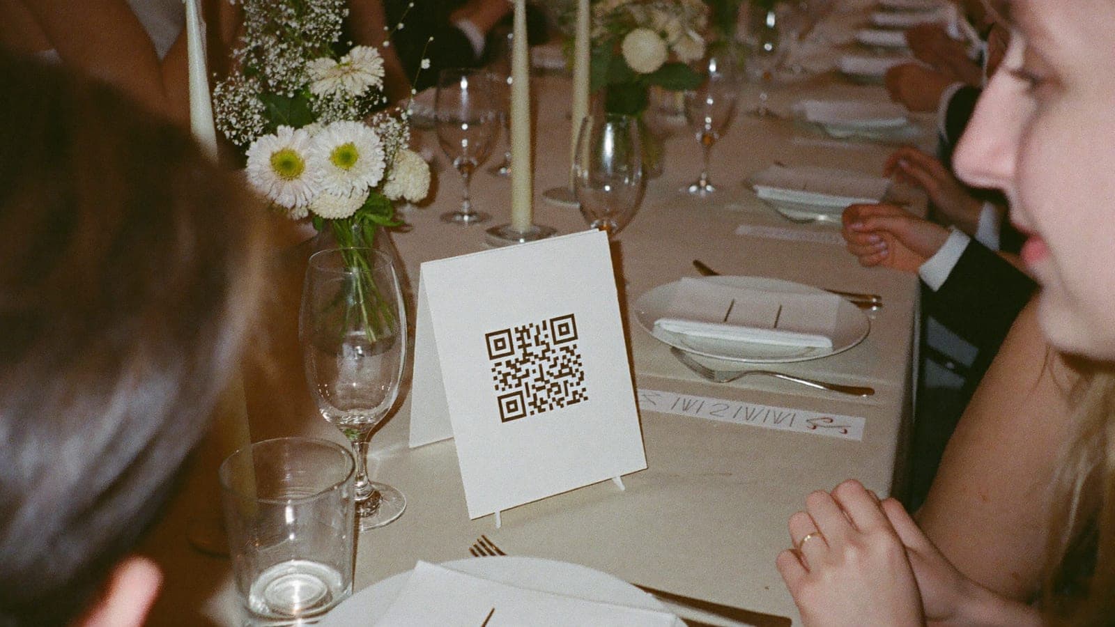 Табличка с QR-кодом между тарелками и цветами на свадебном столе