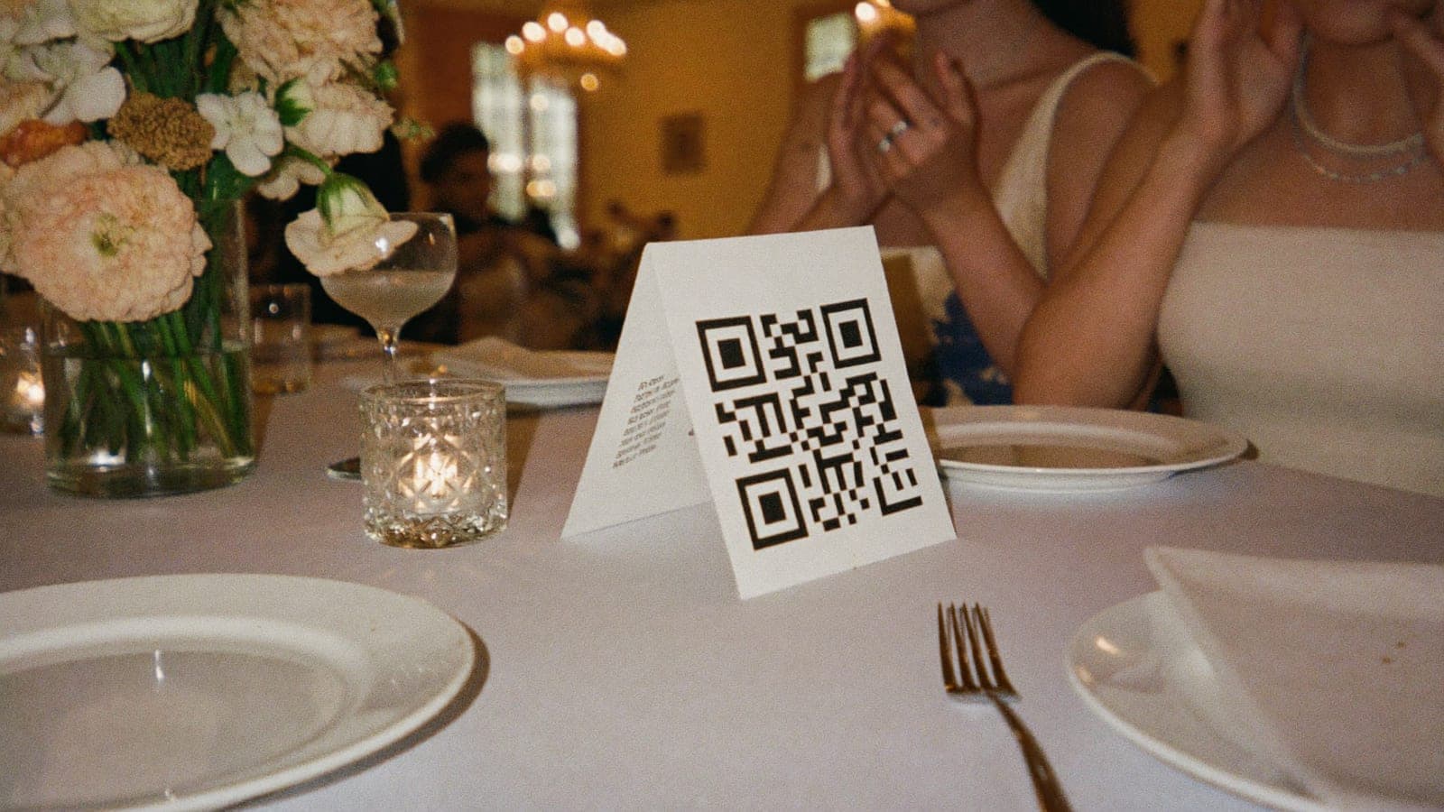 Düğün masasında tabaklar ve çiçekler arasında QR kodlu bir masa kartı