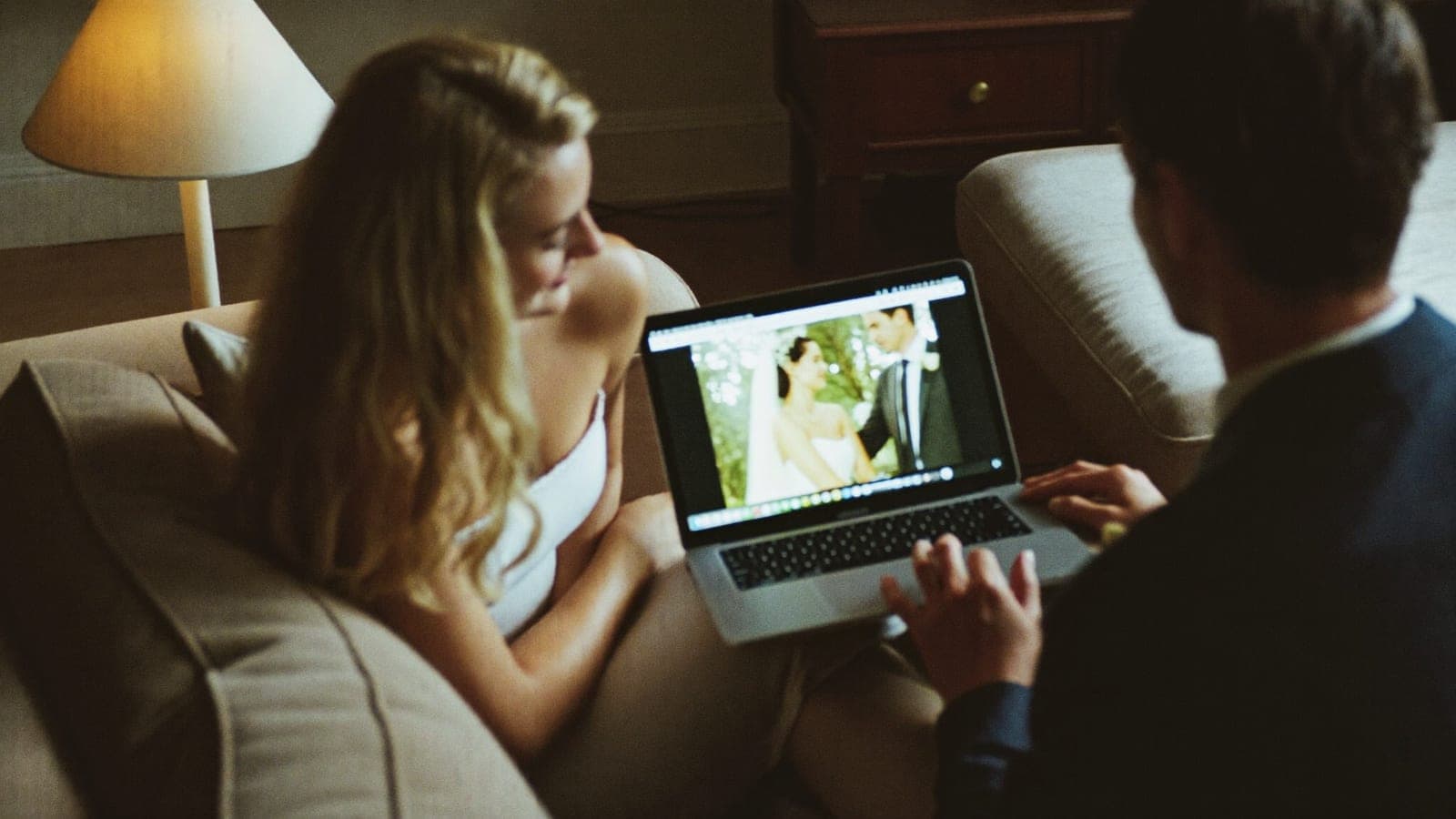 An engaged couple on the sofa with a laptop, planning their wedding