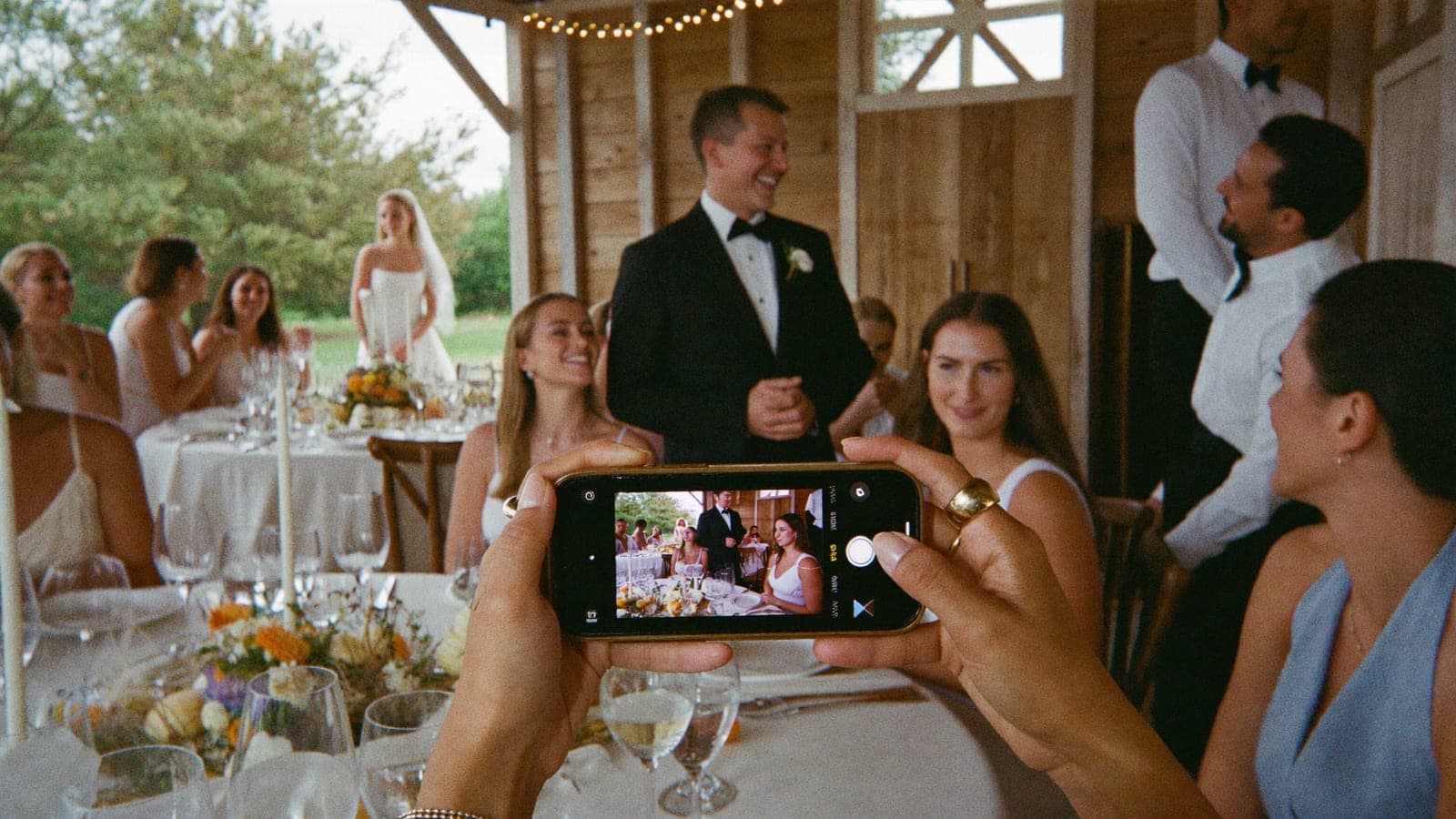 A guest films the best man's speech on a phone during dinner